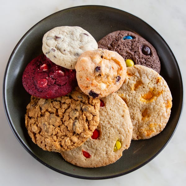 A dark plate holds a variety of Alexandria Pastry Shop cookies, including chocolate chip, red velvet, and oatmeal.