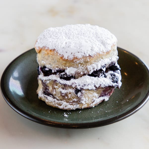 A blueberry scone from Alexandria Pastry Shop, dusted with powdered sugar, on a dark green plate.