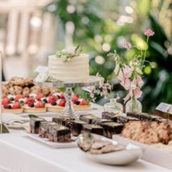 A white frosted cake on a stand surrounded by fruit tarts, brownies, and cookies.