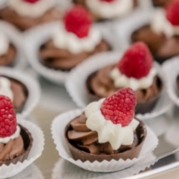 Chocolate tarts with whipped cream and a fresh raspberry on top, arranged on a silver tray.