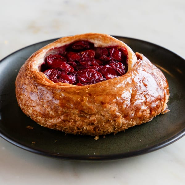 A golden-brown pastry filled with glistening red cherries sits on a dark plate.