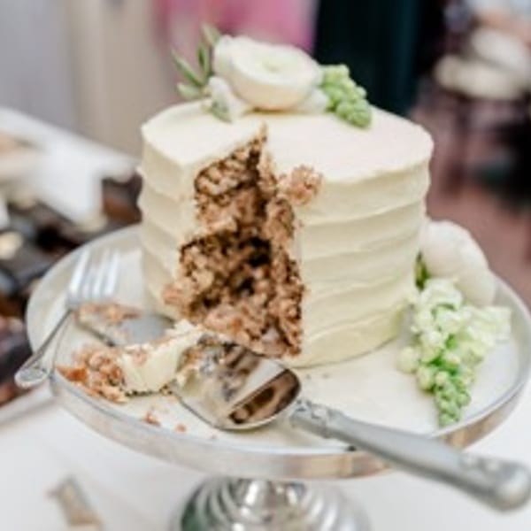 A partially eaten cake with white frosting and floral decorations on a silver cake stand.