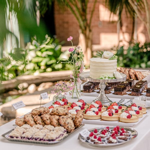 A dessert table with a white cake, chocolate bars, fruit tarts, cookies, and berry crumble.
