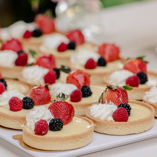 Rows of Alexandria Pastry Shop fruit tarts with strawberries, raspberries, blackberries, and whipped cream.