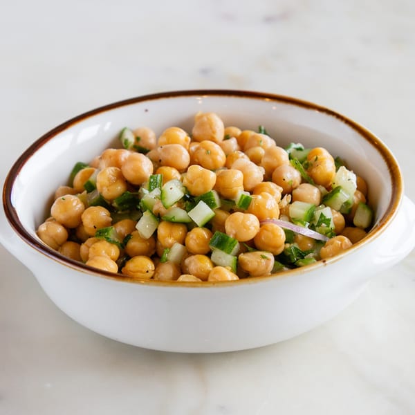A white bowl filled with chickpea salad, diced cucumbers, and red onions.